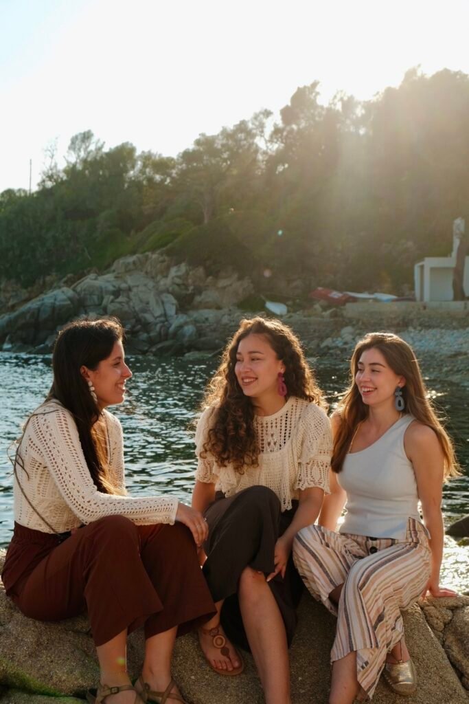 Three women wearing Hibiscus Amarillo handcrafted earrings from the Costa Brava in Bloom collection, standing together by the Mediterranean Sea.